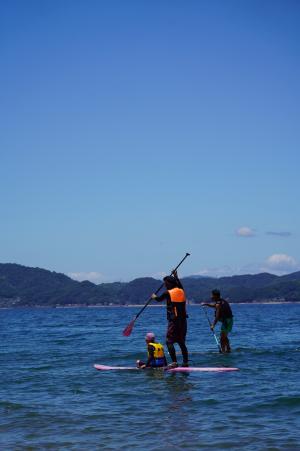 青い空と海を背景にサップに乗る親子が移っている写真